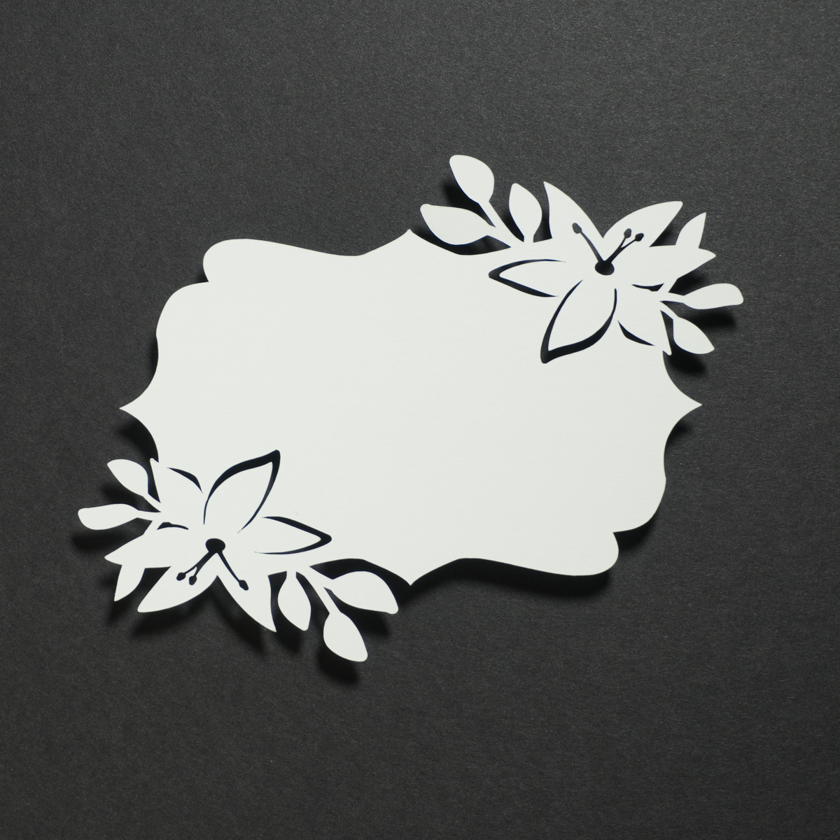 Lily lace-cut paper: a white scalloped tag with cut-out lily flowers in two corners