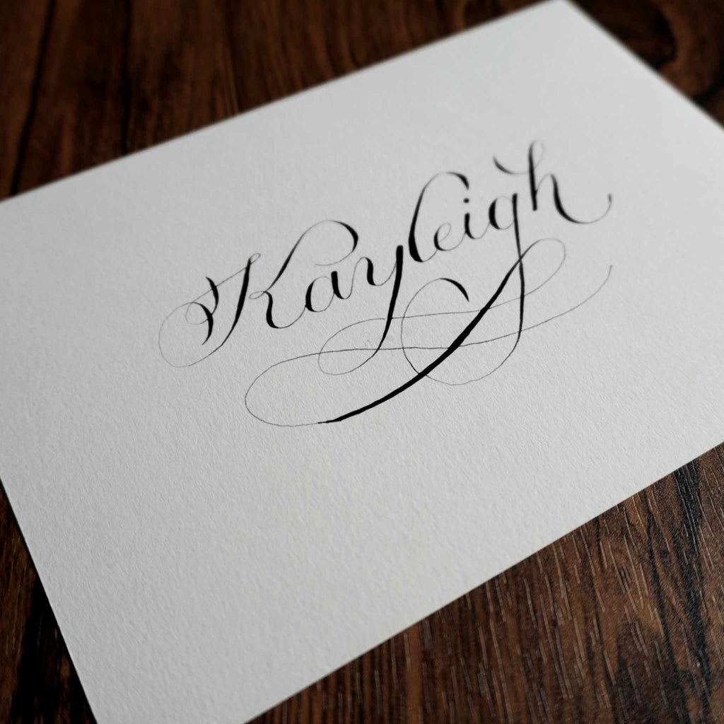 Copperplate calligraphy name card at an angle on a dark wood table
