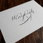 Copperplate calligraphy name card at an angle on a dark wood table
