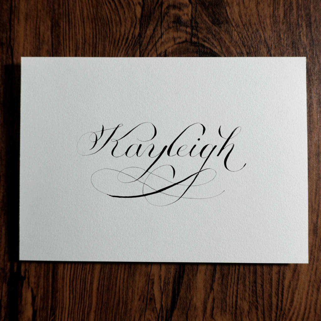 Custom name calligraphy card with a flourished "Kayleigh" on a wood background