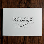 Custom name calligraphy card with a flourished "Kayleigh" on a wood background