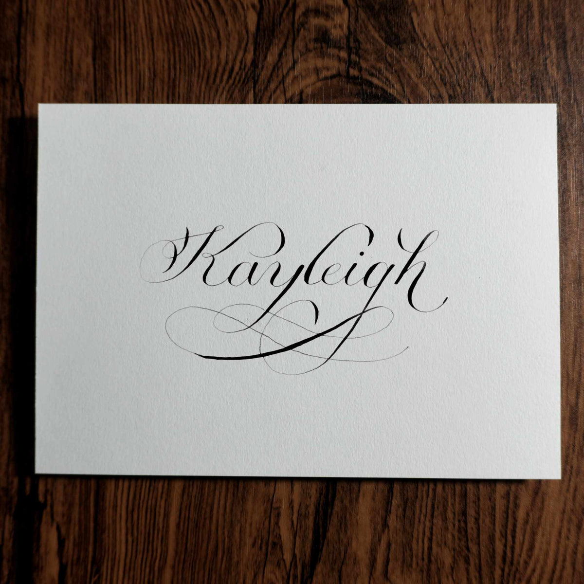 Custom name calligraphy card with a flourished "Kayleigh" on a wood background
