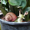 Articulated snail 3D print with a brown spiral shell and green body in a potted plant