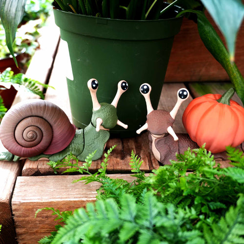 Two 3D-printed snails on a garden step, one with a removable pumpkin shell