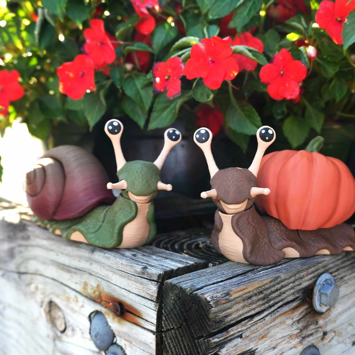 Green snail with a spiral shell and brown snail with a pumpkin shell on a weathered wood planter