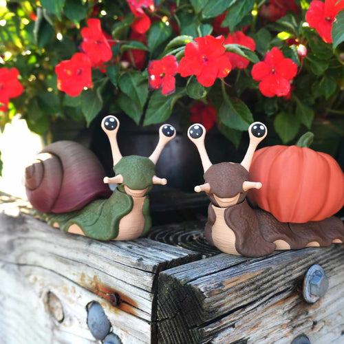 Green snail with a spiral shell and brown snail with a pumpkin shell on a weathered wood planter